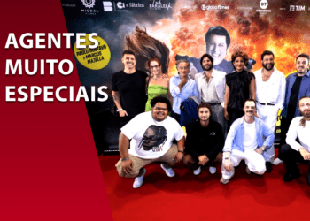 Elenco e equipe do filme "Agentes Muito Especiais" reunidos em um tapete vermelho à frente de um painel promocional com explosões e o rosto de Paulo Gustavo ao fundo. À esquerda, uma faixa vermelha com o título da comédia policial nacional.