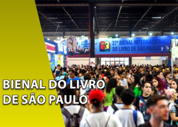 Grande multidão de pessoas circulando entre estantes de livros em um pavilhão de exposições. À esquerda, uma faixa amarela inclinada com o texto "BIENAL DO LIVRO DE SÃO PAULO".