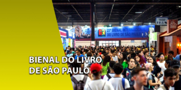 Grande multidão de pessoas circulando entre estantes de livros em um pavilhão de exposições. À esquerda, uma faixa amarela inclinada com o texto "BIENAL DO LIVRO DE SÃO PAULO".