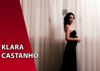 A atriz Klara Castanho vestindo um tomara-que-caia preto, posicionada à frente de uma cortina branca translúcida. À esquerda, uma faixa vermelha inclinada com o texto "KLARA CASTANHO".