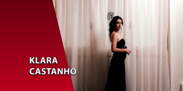 A atriz Klara Castanho vestindo um tomara-que-caia preto, posicionada à frente de uma cortina branca translúcida. À esquerda, uma faixa vermelha inclinada com o texto "KLARA CASTANHO".