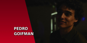 Retrato em baixa luminosidade do ator Pedro Goifman sorrindo levemente. À esquerda, uma faixa vermelha inclinada com o texto "PEDRO GOIFMAN".