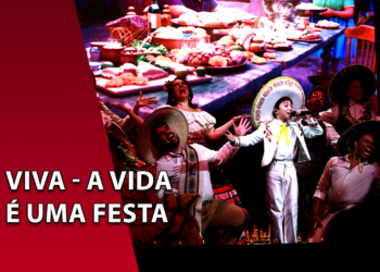 Elenco de músicos e cantores caracterizados com trajes típicos mexicanos e sombreros em uma performance teatral. À esquerda, uma faixa vermelha inclinada com o texto "VIVA - A VIDA É UMA FESTA".