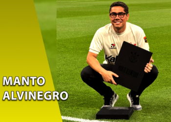 Homem sorridente ajoelhado em um campo de futebol, vestindo uma camisa branca retrô do Corinthians e segurando o livro "Manto Alvinegro". À esquerda, uma faixa amarela inclinada com o texto "MANTO ALVINEGRO".