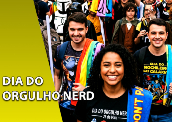 Grupo de jovens sorridentes caminhando em uma parada com toalhas nos ombros e sabres de luz. À esquerda, uma faixa amarela inclinada com o texto "DIA DO ORGULHO NERD".