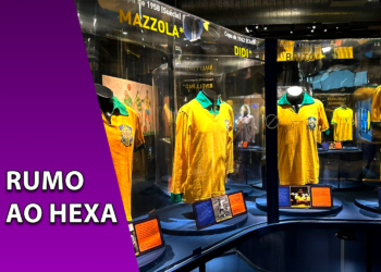 Camisas históricas amarelas da Seleção Brasileira expostas em vitrines de vidro iluminadas dentro de um museu com nomes de jogadores antigos. À esquerda, uma faixa roxa inclinada com o texto "RUMO AO HEXA".