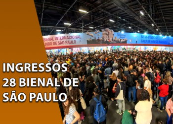 Visão panorâmica dos pavilhões da Bienal do Livro repleta de visitantes e uma grande multidão caminhando diante de stands iluminados. À esquerda, uma faixa marrom inclinada com o texto "INGRESSOS 28 BIENAL DE SÃO PAULO".