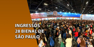 Visão panorâmica dos pavilhões da Bienal do Livro repleta de visitantes e uma grande multidão caminhando diante de stands iluminados. À esquerda, uma faixa marrom inclinada com o texto "INGRESSOS 28 BIENAL DE SÃO PAULO".